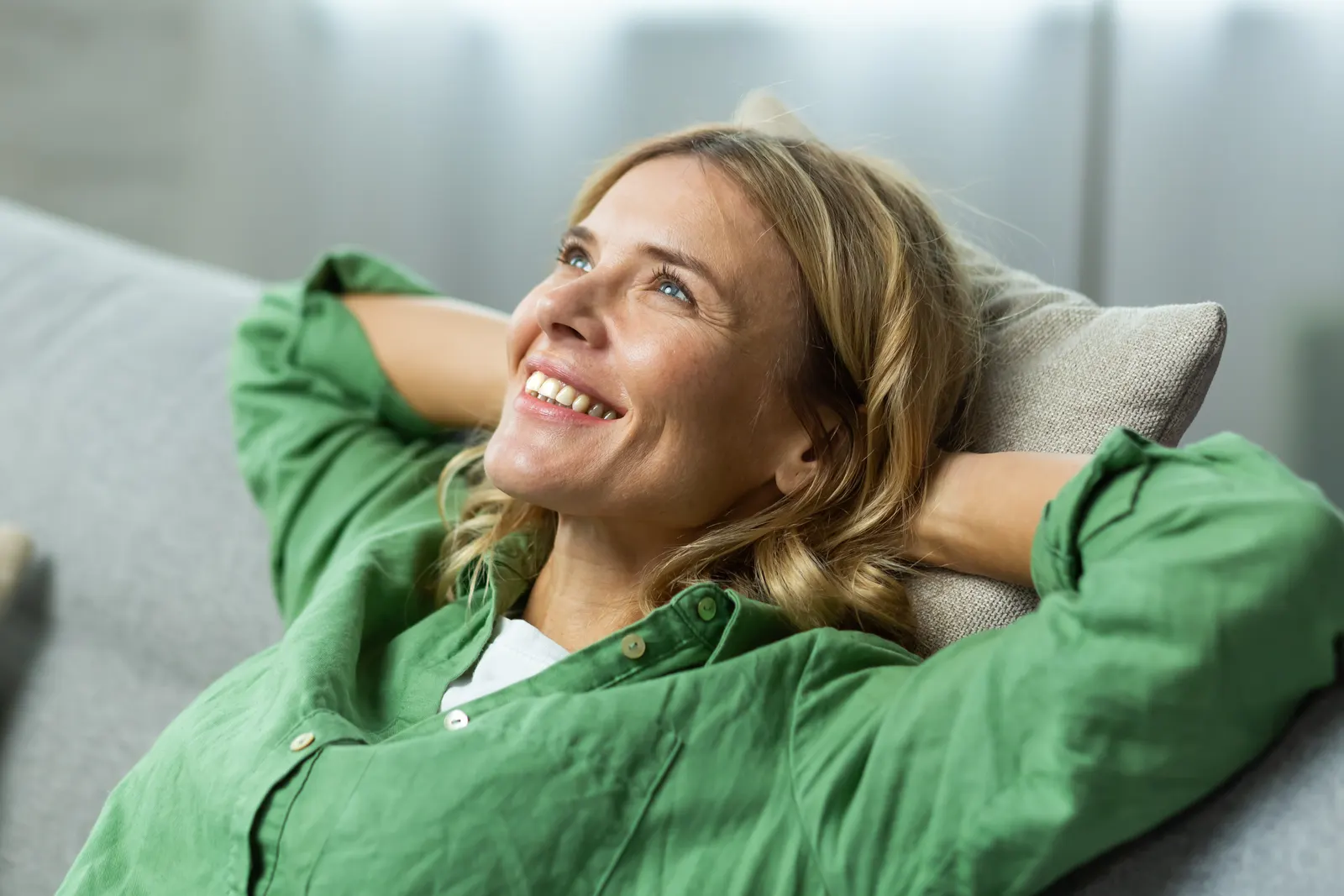 Smiling woman in a green shirt relaxing on a sofa at home